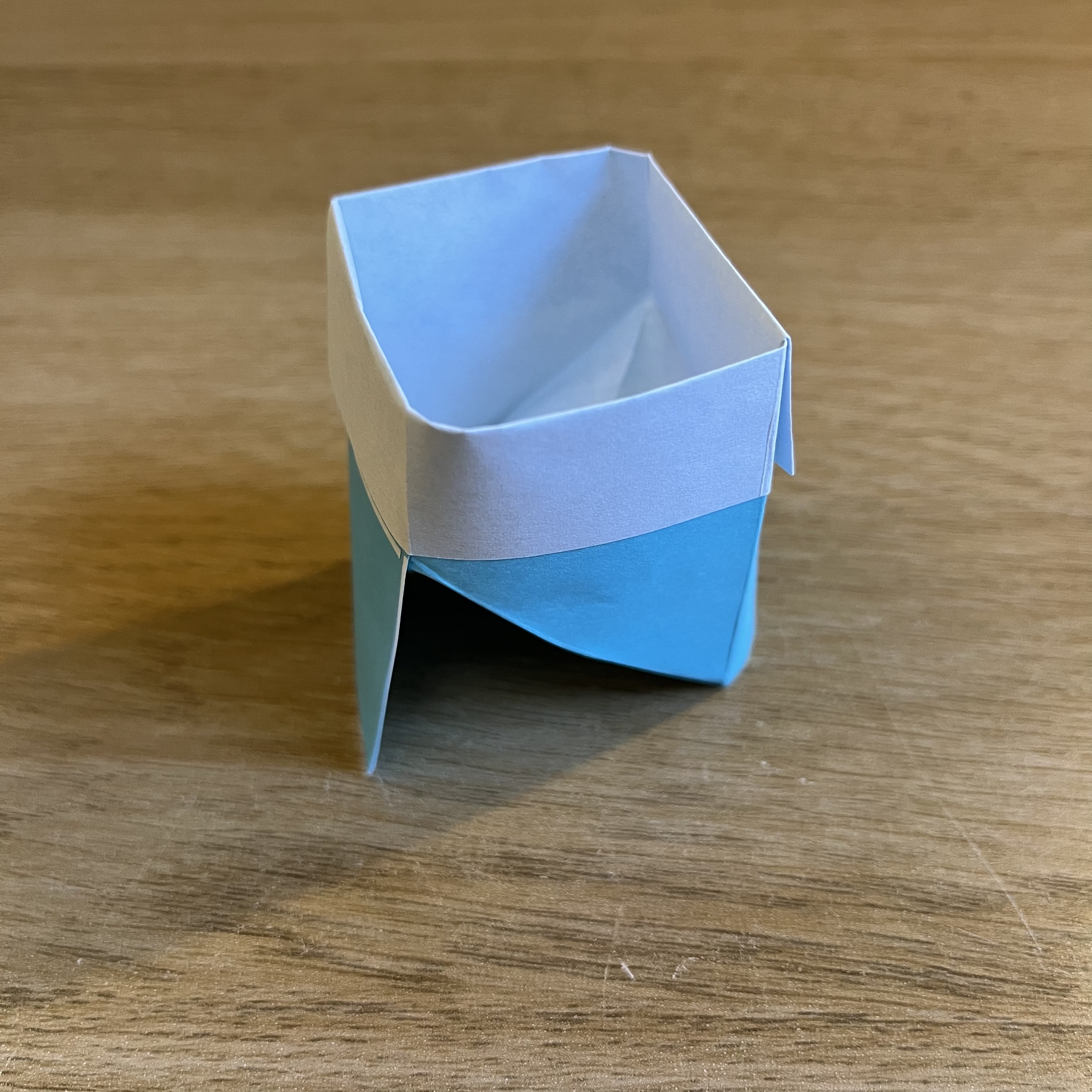 A blue and white origami cup on a wooden table.