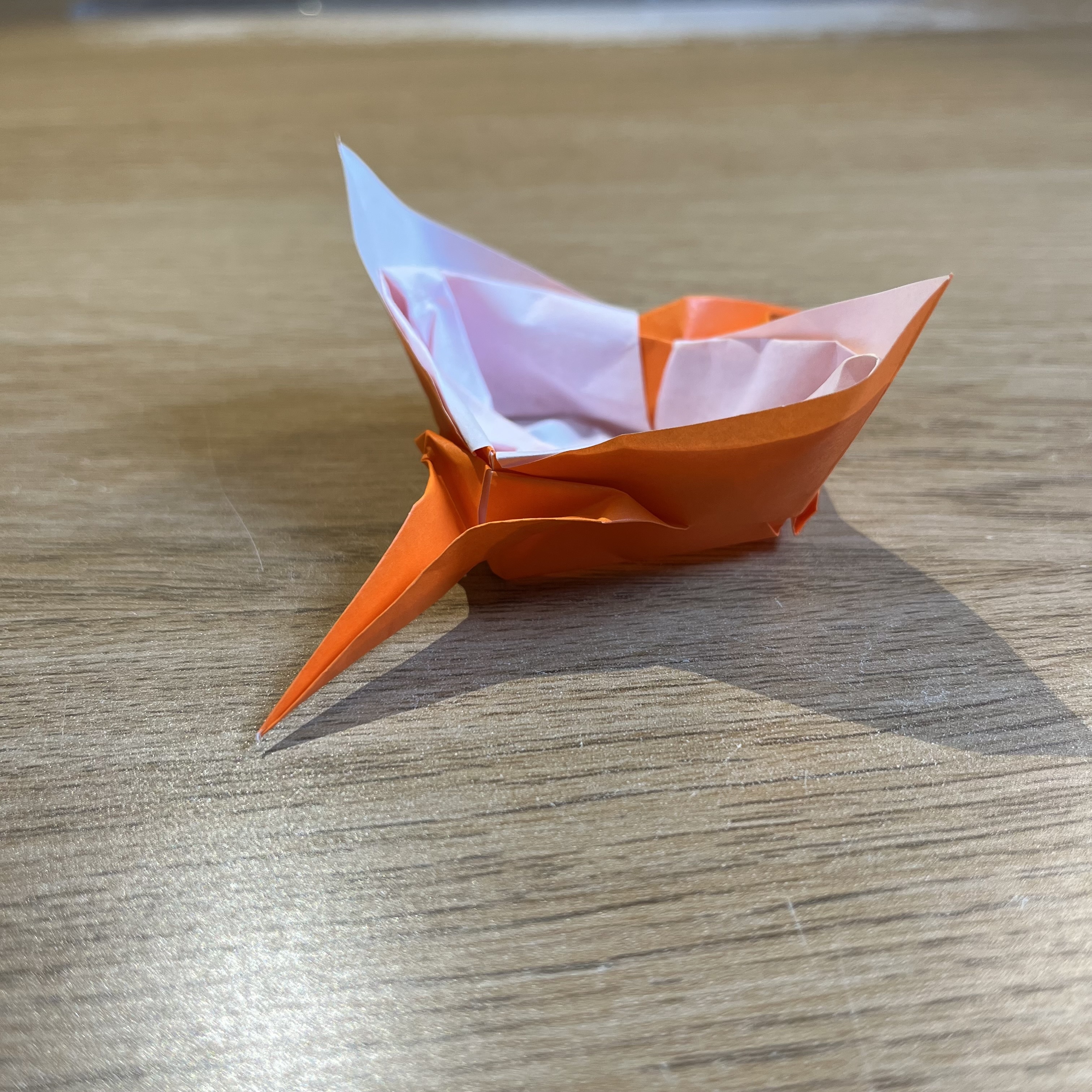 An orange and white origami boat rests on a wooden surface.