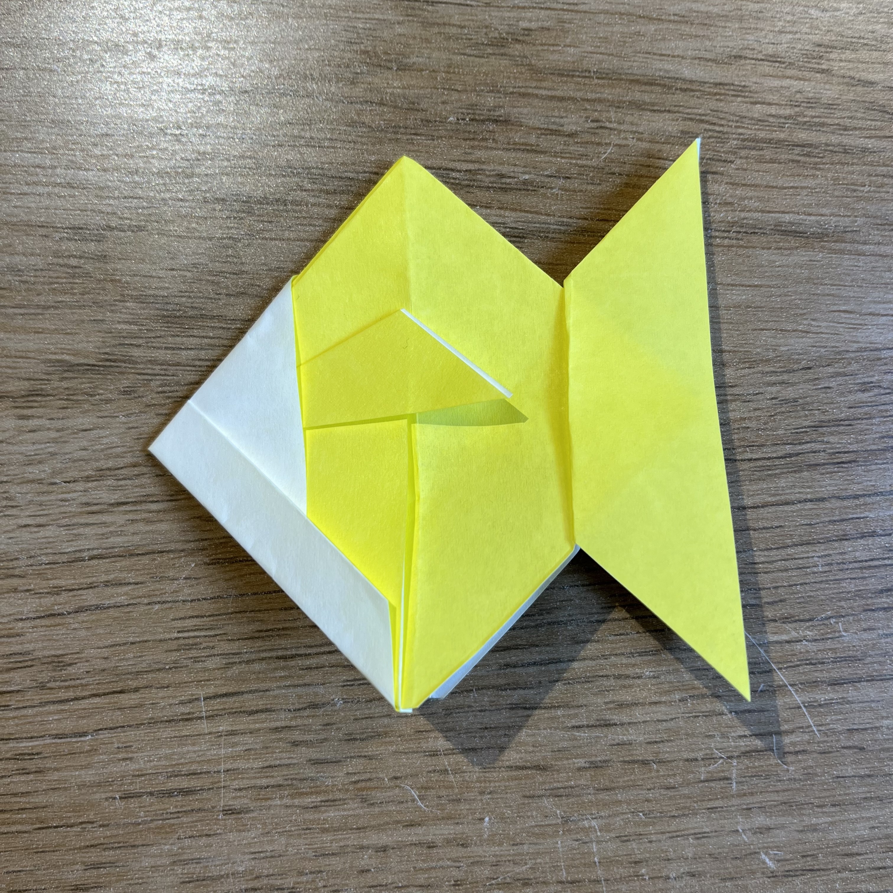 A yellow origami fish on a wooden table.