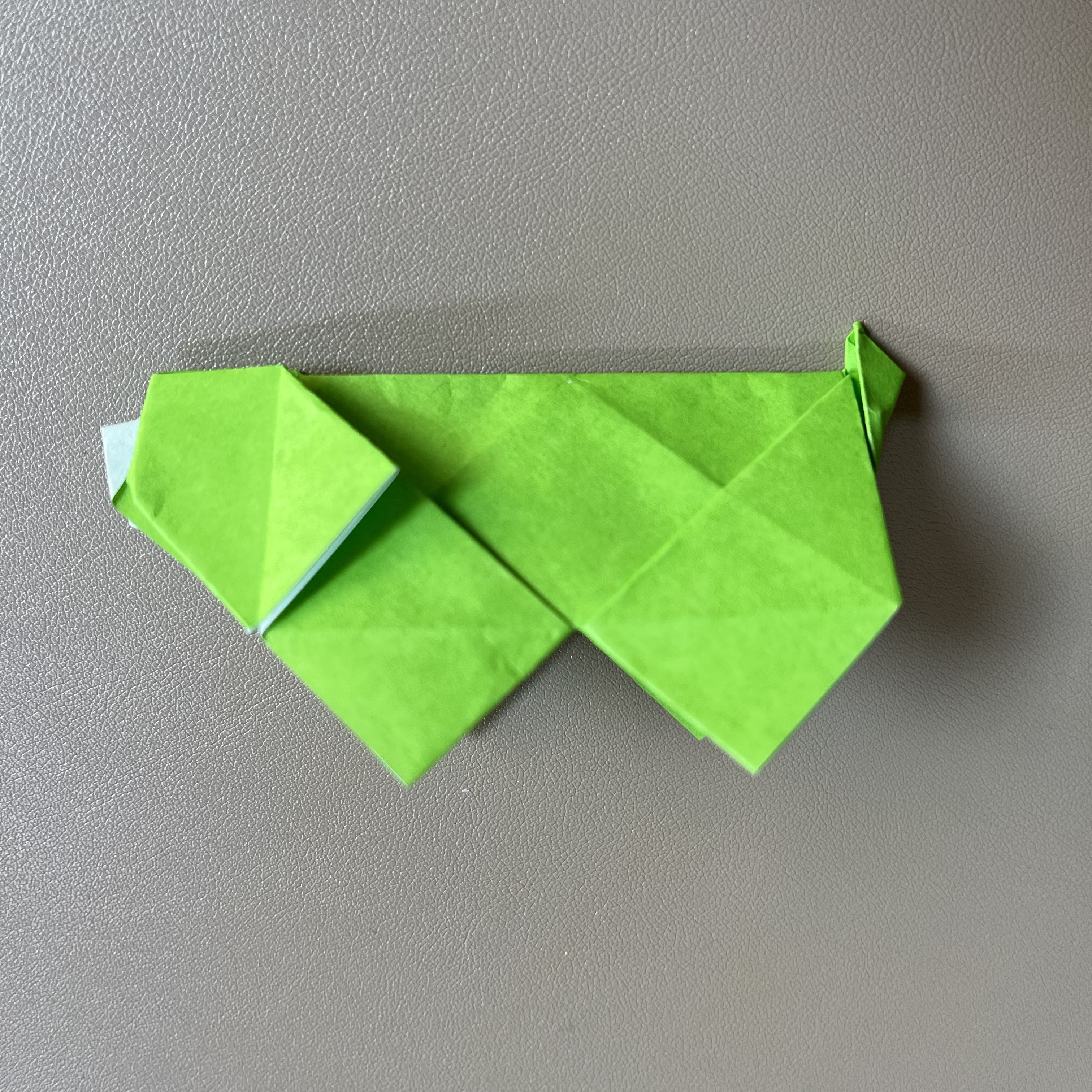 A green origami hot with geometric folds displayed on a grey surface. the hog's body is stylized with a pointed tail and flippers.