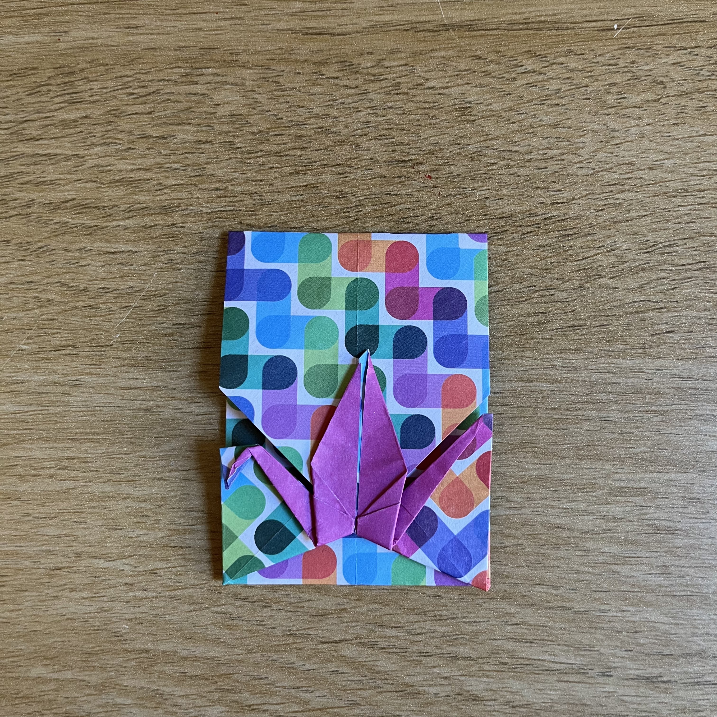 An origami crane envelope  folded from a patterned square of paper. The pattern includes various shades of blue, green, red, purple, and yellow. Shown closed.