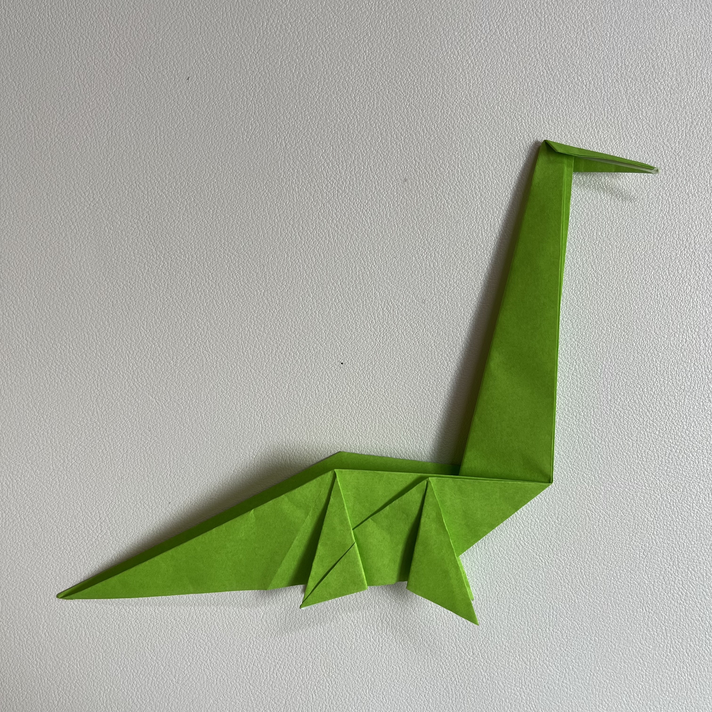 A green origami dinosaur on a white table.