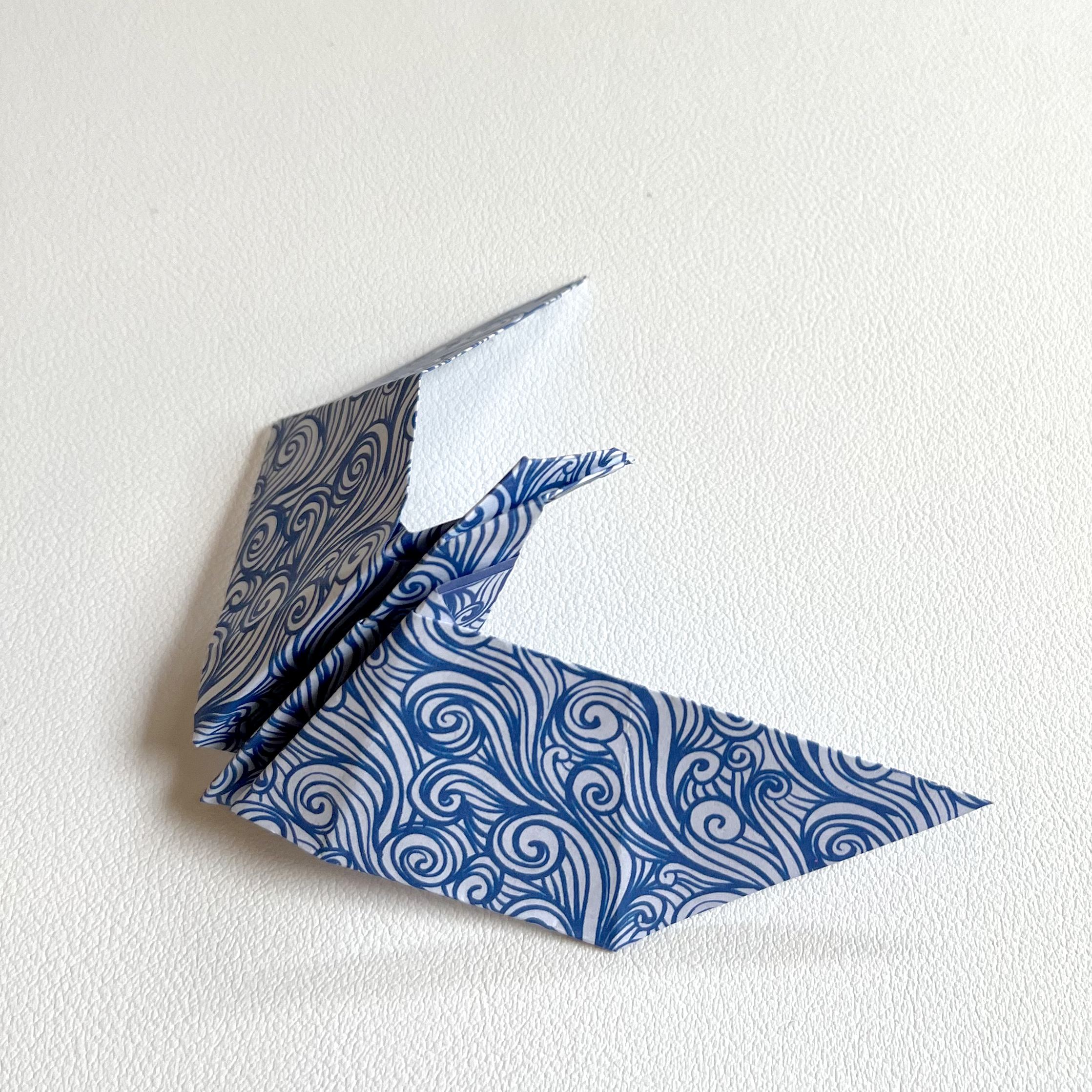 A blue and white origami bird on a white surface.