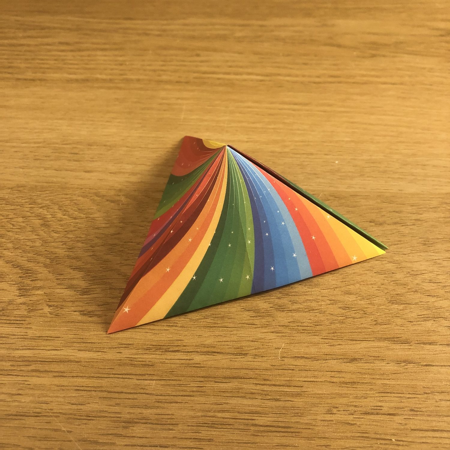 A rainbow colored triangular object on a wood surface.
