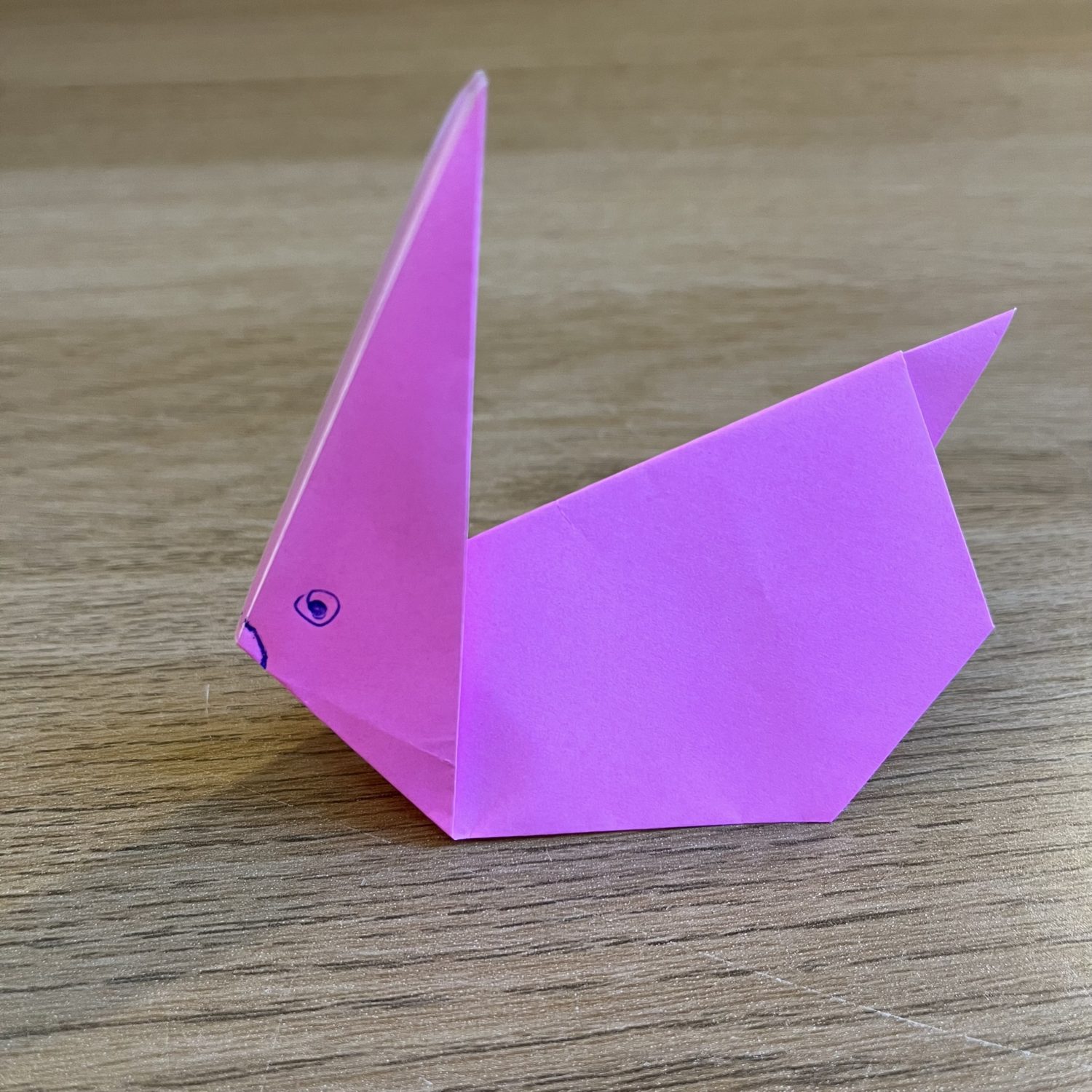 A solitary pink origami paper bunny set placed on a wooden surface.