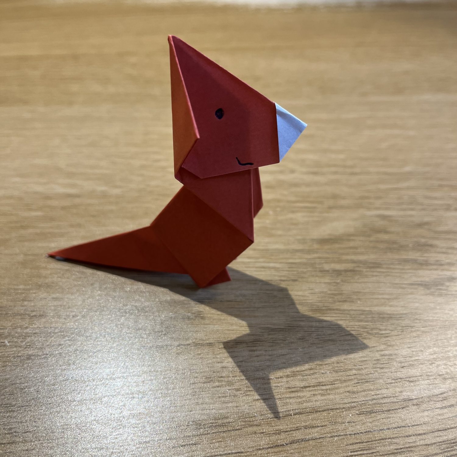 A red origami kangaroo sitting on a wooden table.