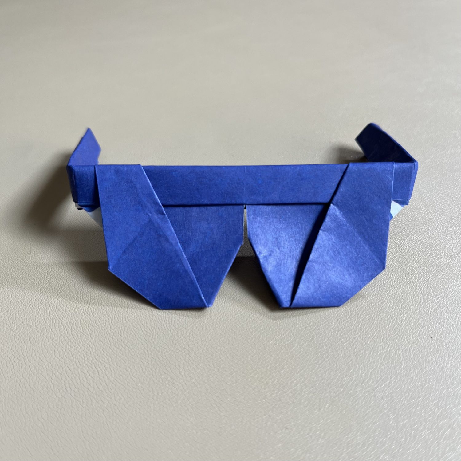 A pair of blue origami glasses on a table.