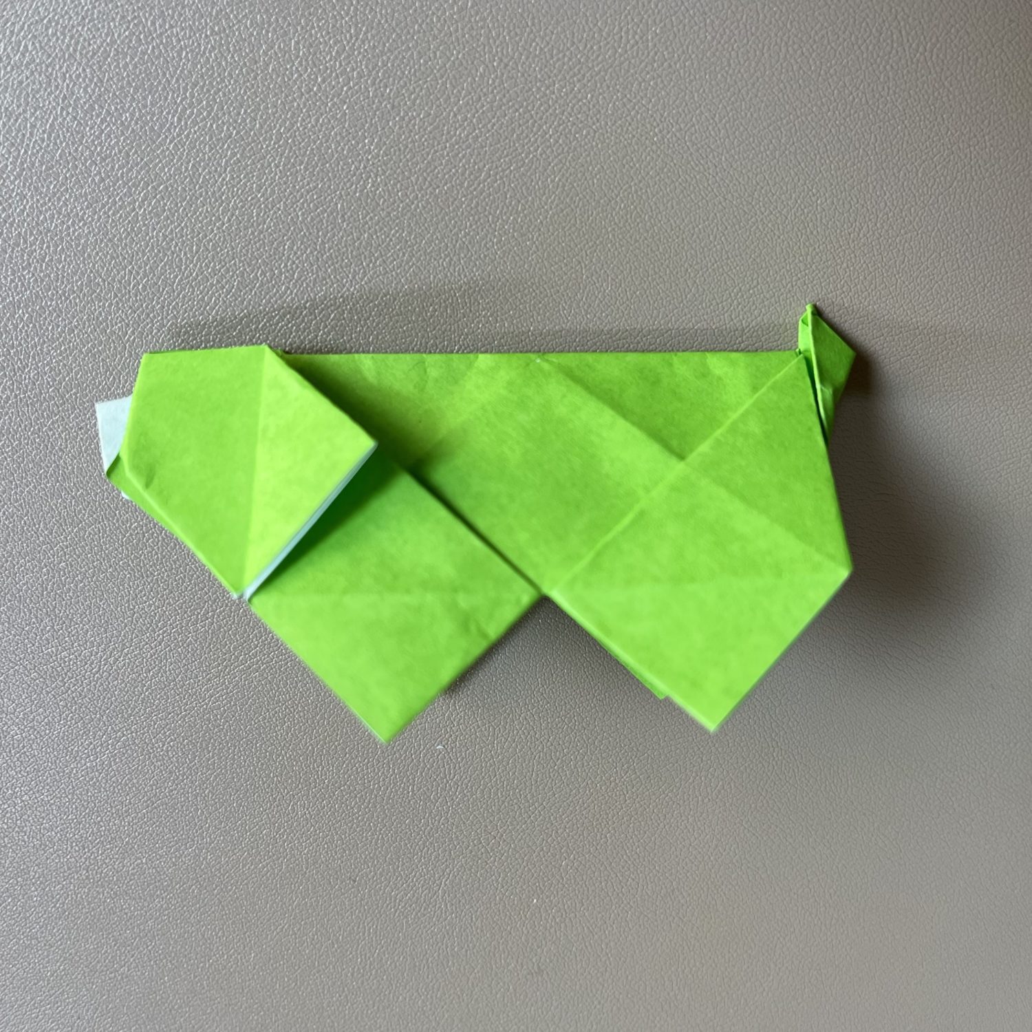 A green origami hot with geometric folds displayed on a grey surface. the hog's body is stylized with a pointed tail and flippers.
