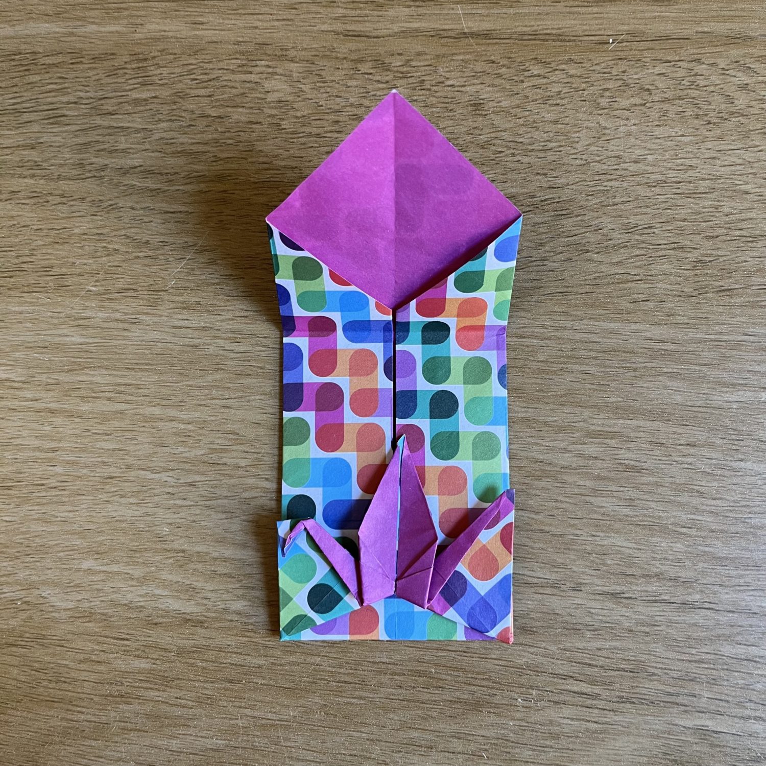 An origami crane envelope  folded from a patterned square of paper. The pattern includes various shades of blue, green, red, purple, and yellow. Shown open.