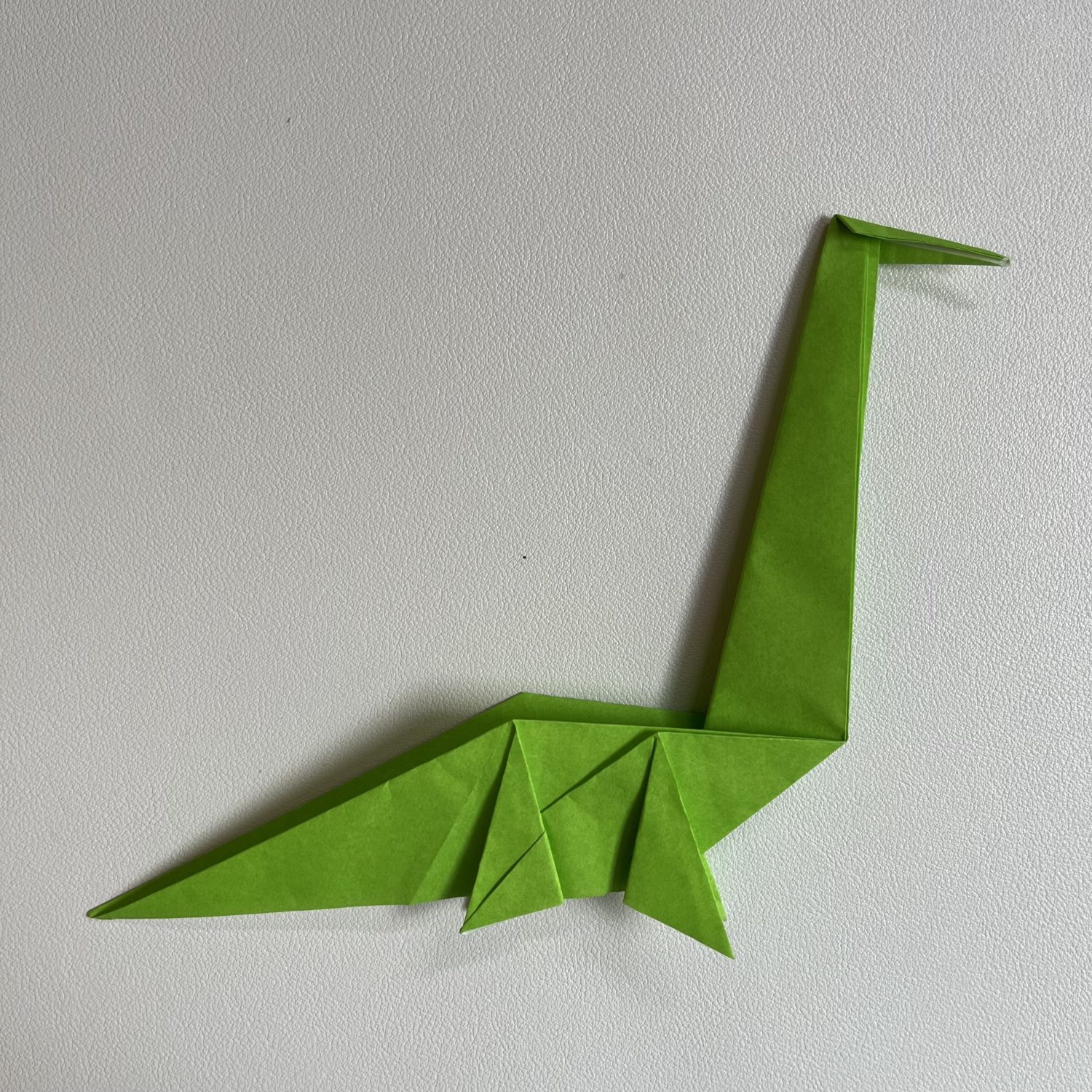 A green origami dinosaur on a white table.