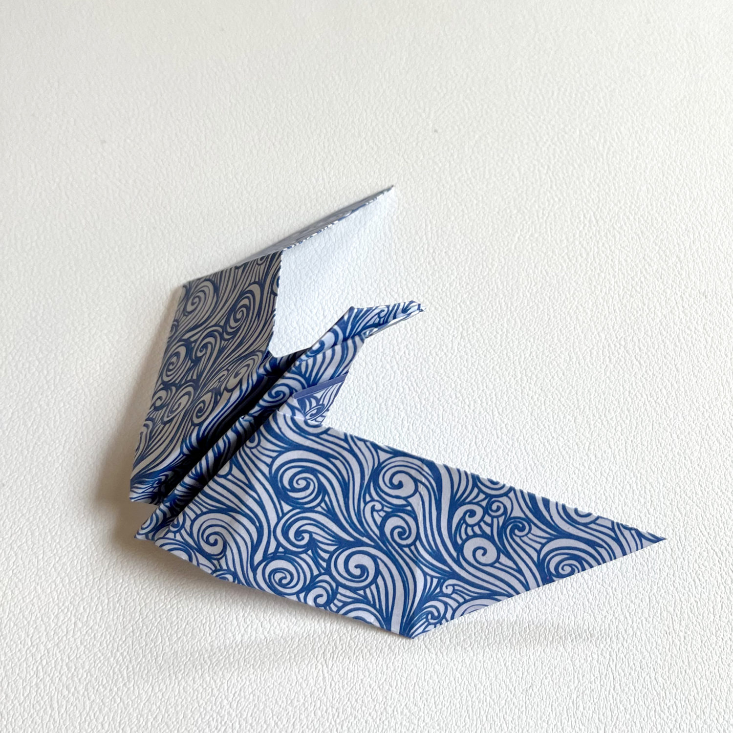 A blue and white origami bird on a white surface.