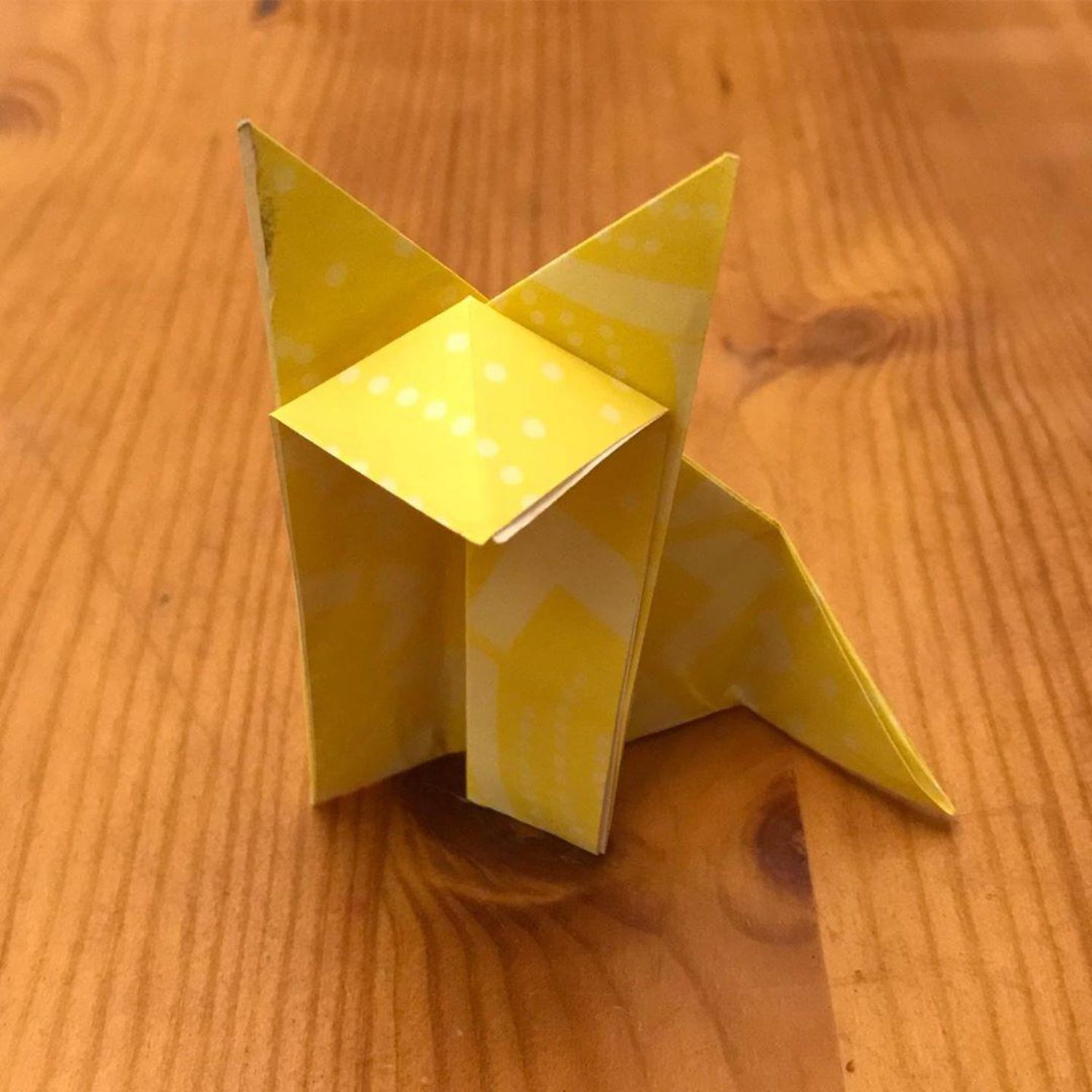 A yellow origami fox sitting on a wooden table.