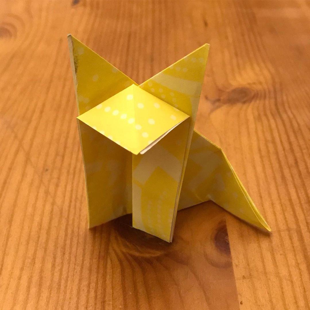 A yellow origami fox sitting on a wooden table.