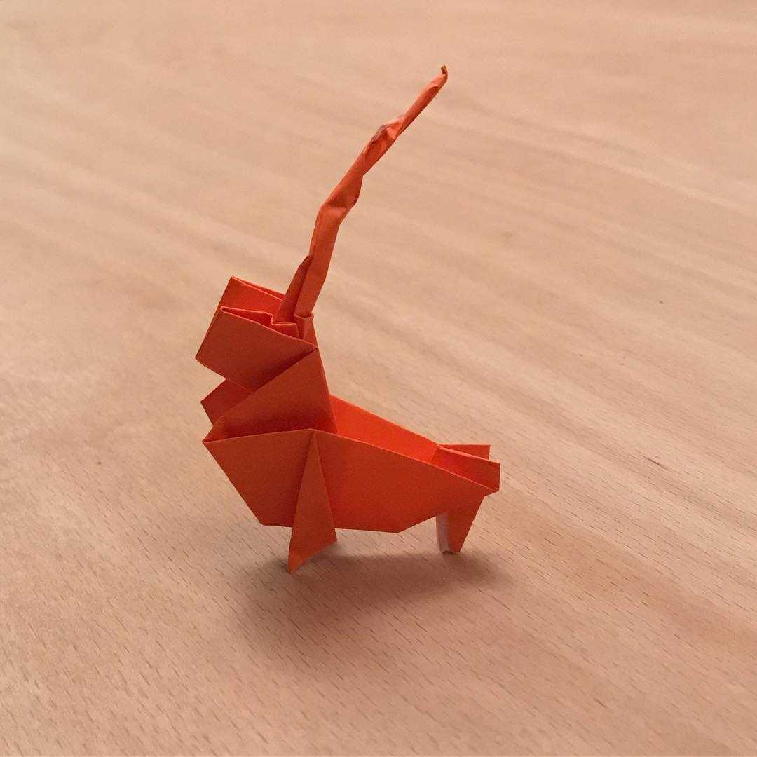 An orange origami paper chirping cricket against a wooden backdrop.